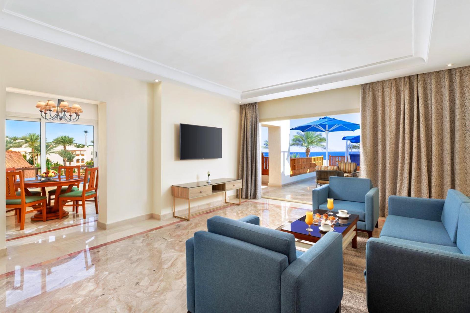 Pickalbatros Royal Grand Sharm - Adults Friendly 16 Years Plus Exteriör bild The photo shows a modern and spacious living area. There are several blue chairs arranged around a coffee table, which holds some refreshments. A large flat-screen TV is mounted on the wall, and there are sliding glass doors that open to an outdoor a