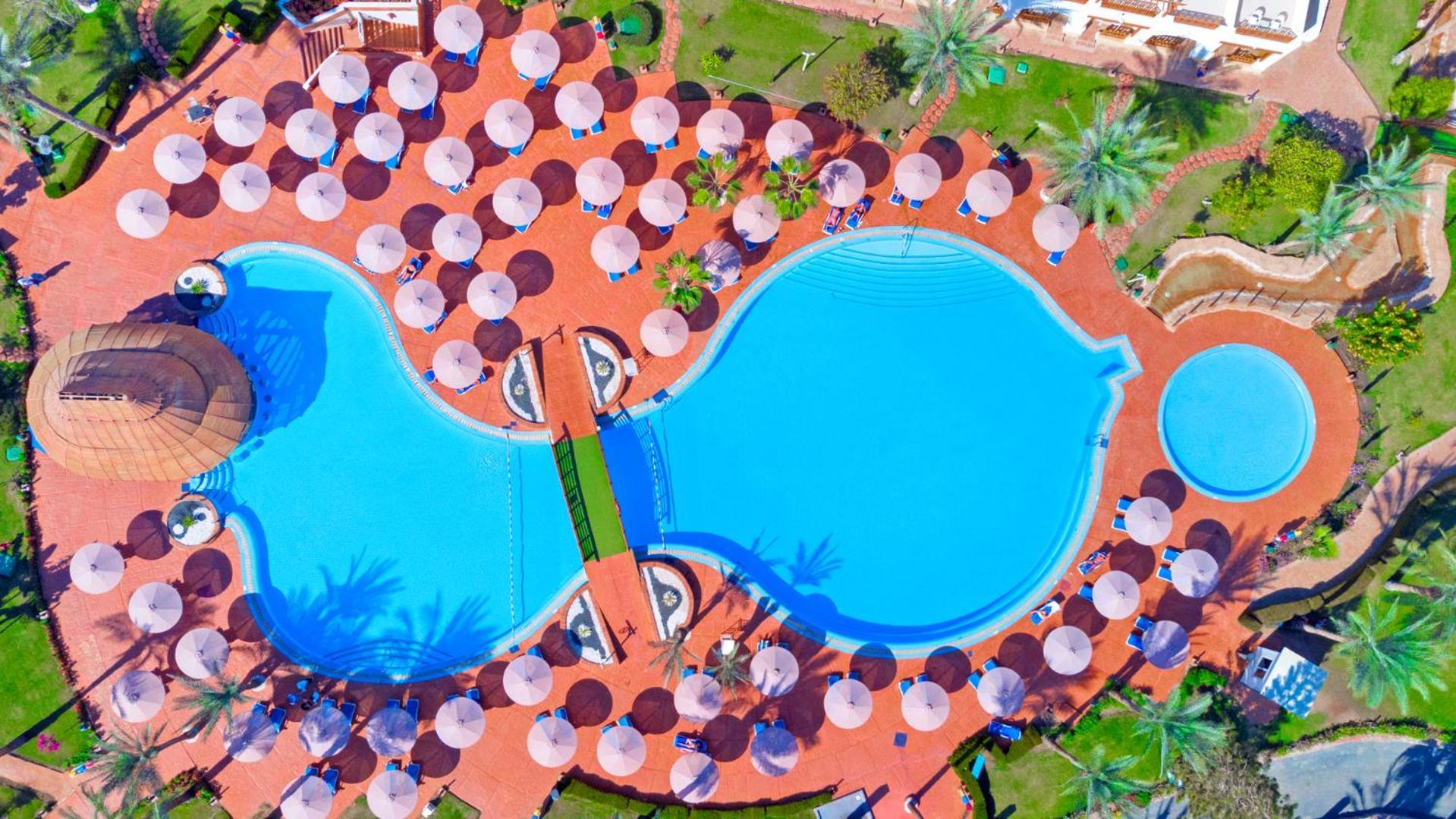 Pickalbatros Royal Grand Sharm - Adults Friendly 16 Years Plus Exteriör bild The photo shows an aerial view of a large swimming pool area, shaped in a distinctive layout resembling two interconnected pools. Surrounding the main pool are numerous umbrellas, providing shade for visitors. The pool area is set on a reddish-colore
