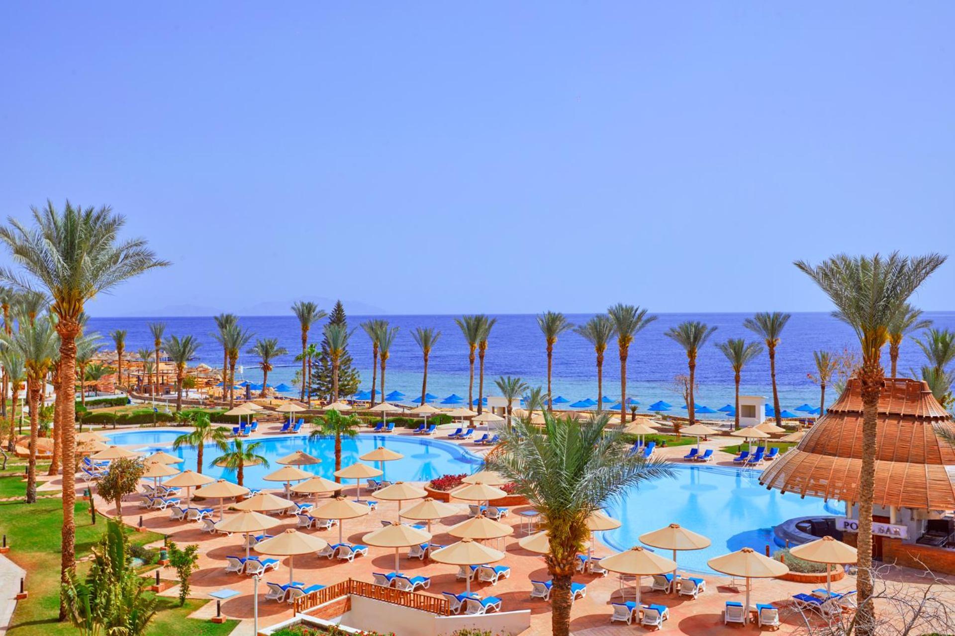 Pickalbatros Royal Grand Sharm - Adults Friendly 16 Years Plus Exteriör bild The photo showcases a beautiful resort setting by the sea. It features a large swimming pool surrounded by sunny lounge chairs and umbrellas, perfect for relaxation. The area is adorned with lush palm trees, adding to the tropical vibe. In the backgr